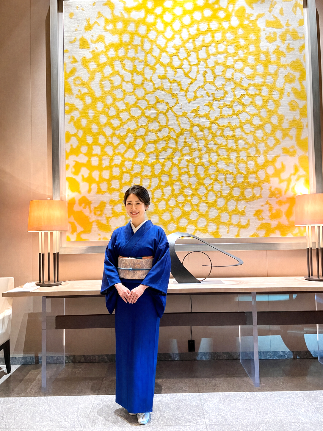 パレスホテル東京のロビーアート前に立つ、前田仁仙のロイヤルブルーの鳳凰文着物の女性。
Woman in a royal blue phoenix-pattern kimono standing before lobby artwork at Palace Hotel Tokyo