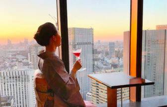 The Okura Tokyo 41階「バーラウンジ スターライト」で、夕景を眺めながらカクテルを愉しむ薄紫の大島紬姿の女性 A woman in a pale purple Oshima tsumugi kimono enjoying a cocktail at sunset at Bar Lounge Starlight on the 41st floor of The Okura Tokyo