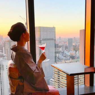 The Okura Tokyo 41階「バーラウンジ スターライト」で、夕景を眺めながらカクテルを愉しむ薄紫の大島紬姿の女性 A woman in a pale purple Oshima tsumugi kimono enjoying a cocktail at sunset at Bar Lounge Starlight on the 41st floor of The Okura Tokyo